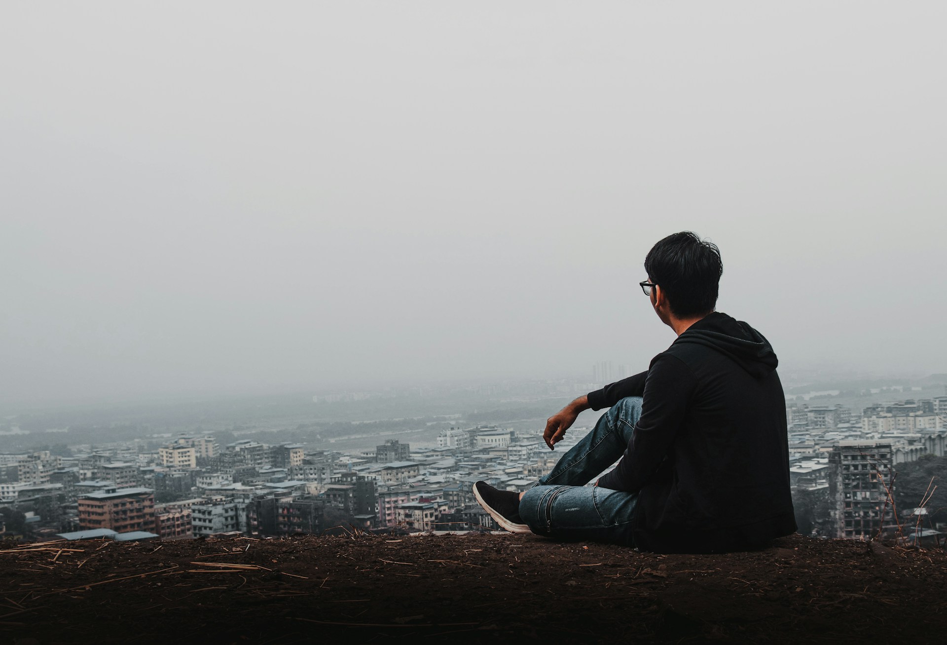 Man in black jacket sitting on brown rock during daytime photo